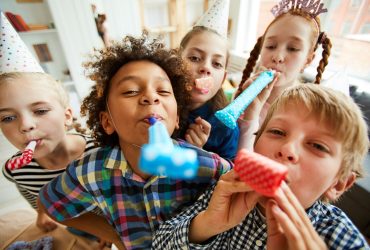 High angle view at multi ethnic group of children blowing party horns at camera